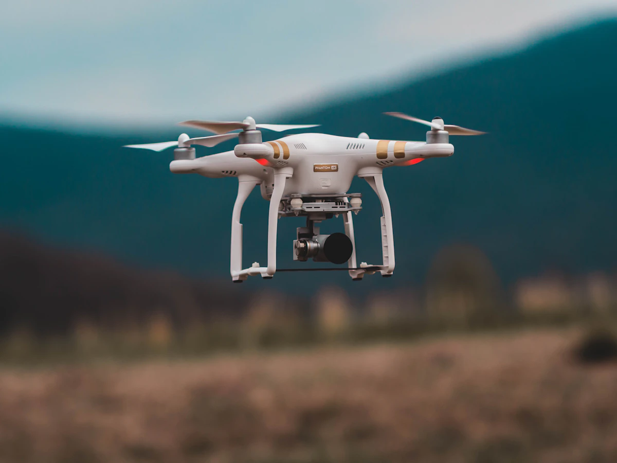 Dron blanco con cámara estabilizada volando sobre un paisaje de colinas al atardecer