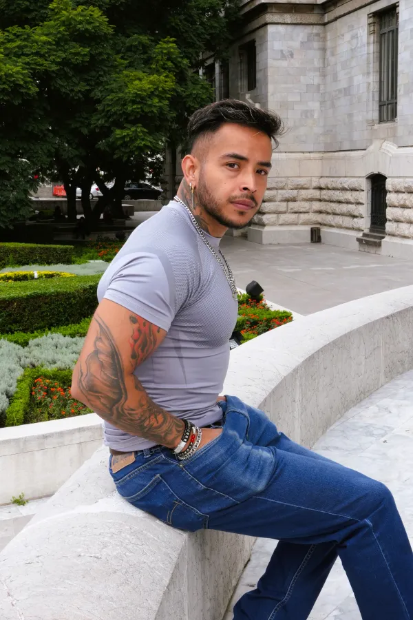Hombre con playera gris sentado en una barda de mármol junto a los jardines de Bellas Artes