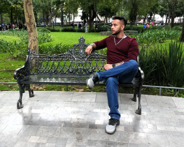 Hombre sentado con las piernas cruzadas en una banca de hierro forjado en la Alameda Central